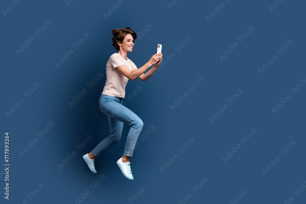 Full body photo of pretty young girl running hold device shopping wear trendy white outfit isolated on dark blue color background