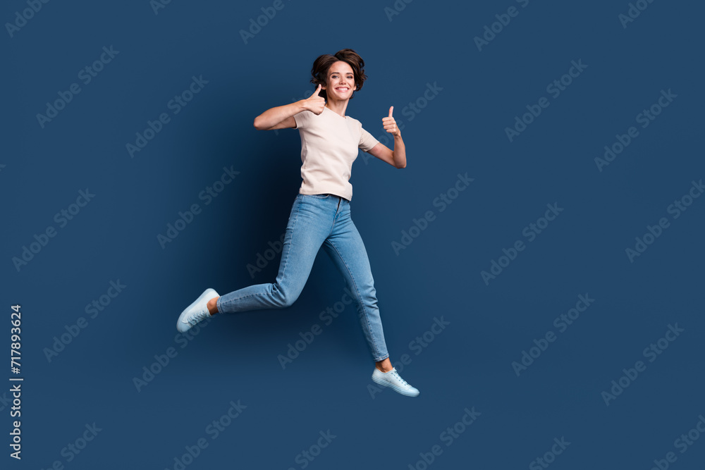 Obraz premium Full length photo of lovely young lady jump run show double thumb up wear trendy white garment isolated on dark blue color background