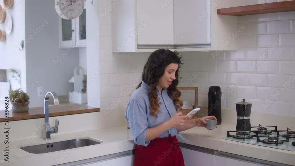 Happy caucasian woman with mobile phone drinking coffee and looking at cell phone screen at home Happy caucasian woman with mobile phone drinking coffee and looking at cell phone screen at home