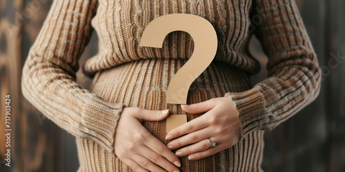 A pregnant woman holding a question mark poster.