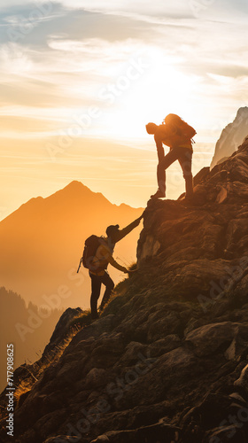 Homem ajudando outro a subir ao topo de uma montanha ao nascer do sol  photo