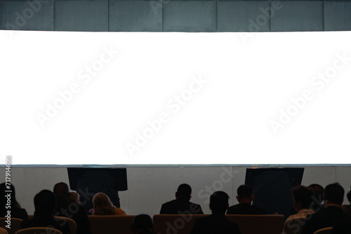Front view of mockup on big blank white screen with space in empty hall with scene and silhouette of audiences