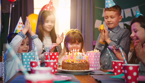 Photography Birthday party of small Caucasian girl blowing candles on the cake and her small friends applauding her and laughing