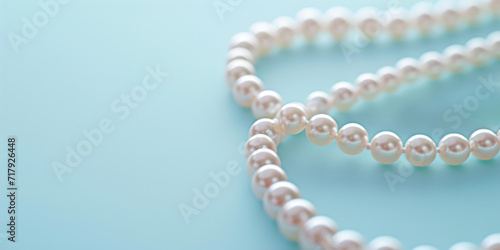 A background with copy space and a string of elegant pearls forms a heart shape on a pastel blue backdrop, providing a sophisticated and romantic setting.
