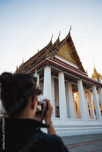 Obraz na płótnie (Selective focus) A defocused tourist is taking pictures at the Wat Ratchanatdaram, a beautiful Buddhist temple that stands proud in the heart of downtown Bangkok, Thailand. w salonie