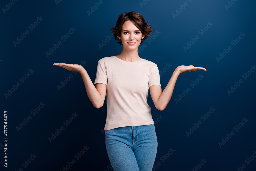 Photo portrait of pretty young girl palm compare hold empty space wear trendy white outfit isolated on dark blue color background Photo portrait of pretty young girl palm compare hold empty space wear trendy white outfit isolated on dark blue color background