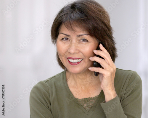 Attractive happy woman looking at camera smiling talking on mobile phone isolated with white wall background closeup.