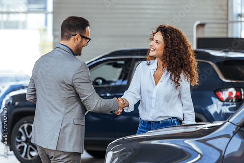 Happy salesman congratulating his female customer for buying a new car in a showroom. Salesperson selling cars at car dealership. © Dragana Gordic