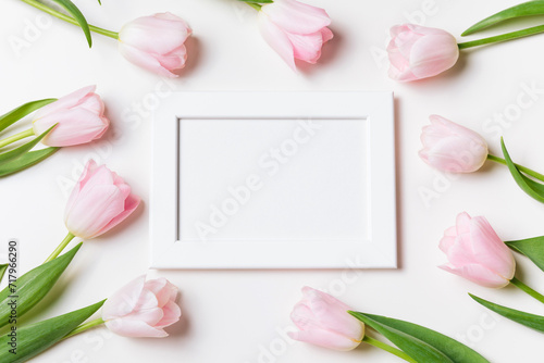 Fototapeta Naklejka Na Ścianę i Meble -  Light pink blooming tulips flowers and white picture frame over white background. Spring holiday banner, happy easter card, mothers day, birthday celebration. Flat lay, top view, copy space