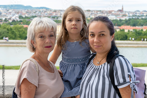 Two women of different ages and a girl pose against the backdrop of Vienna architecture, looking at the camera. Concept: family photo, grandmother, daughter, and granddaughter.