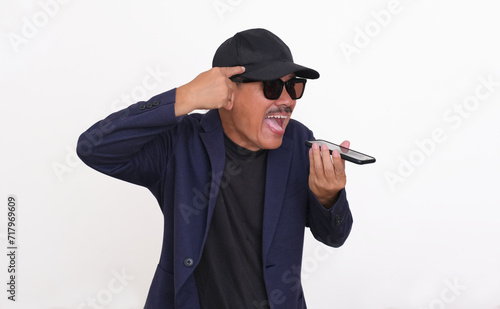A man wearing a dark blazer over a black t-shirt, hat and sunglasses shouted on a smartphone while pointing at his forehead  mad, upset, desperate expression © Bunda