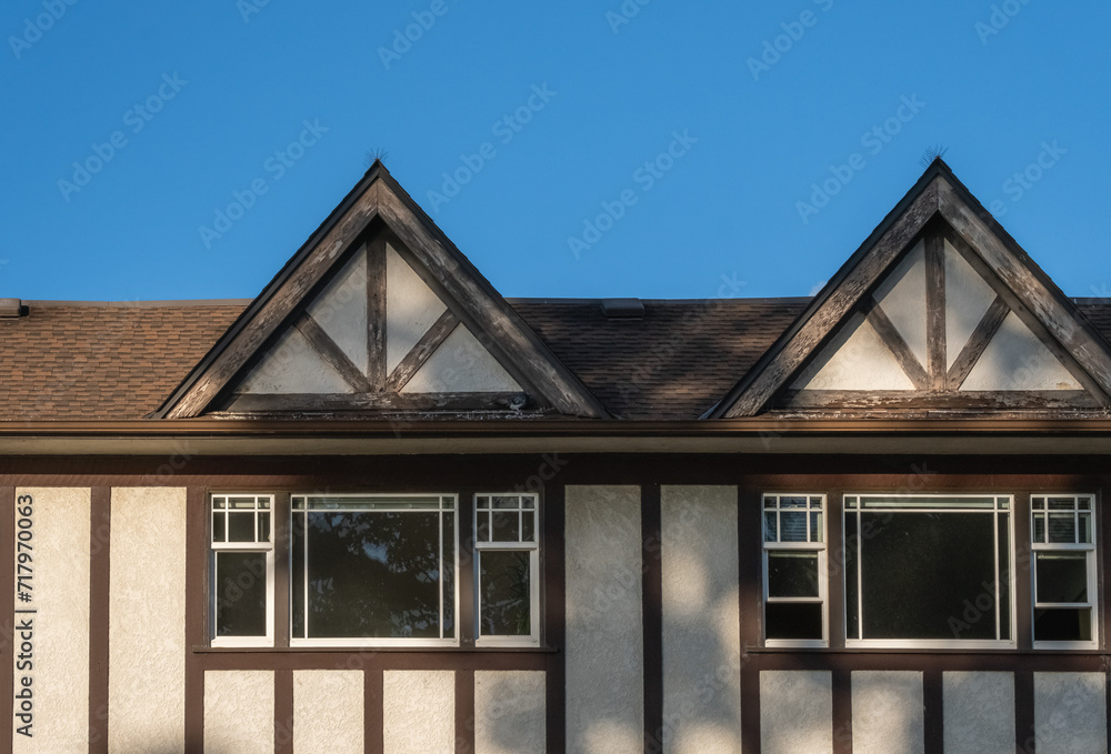 The roof of the house with nice windows. House with shingle roof against blue sky. Windows of a house and facade