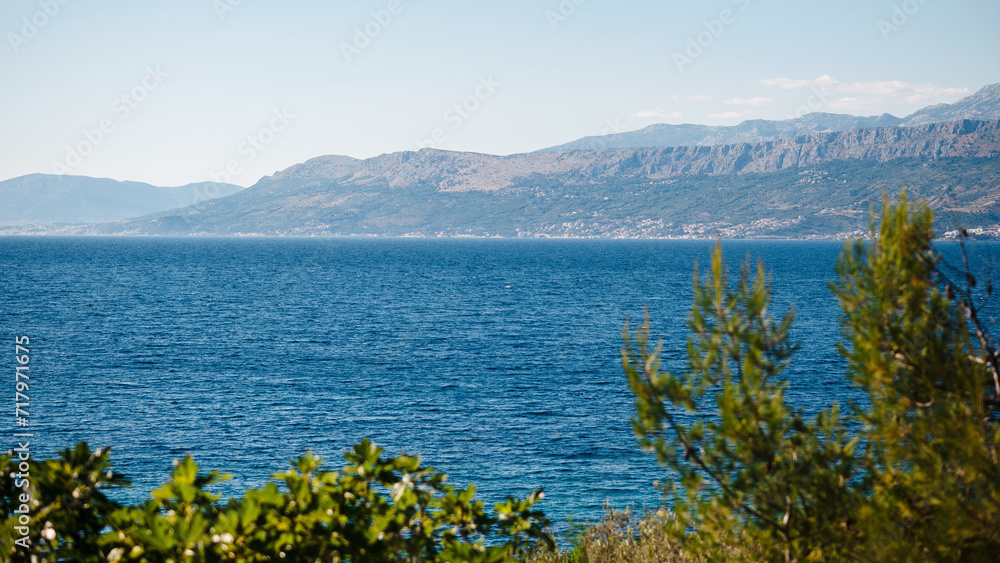 Green tree tops with panoramic view on coast of Brac island. Fascinating landscape of beautiful clear Adriatic sea and high rocky mountains. Atmosphere of calmness.