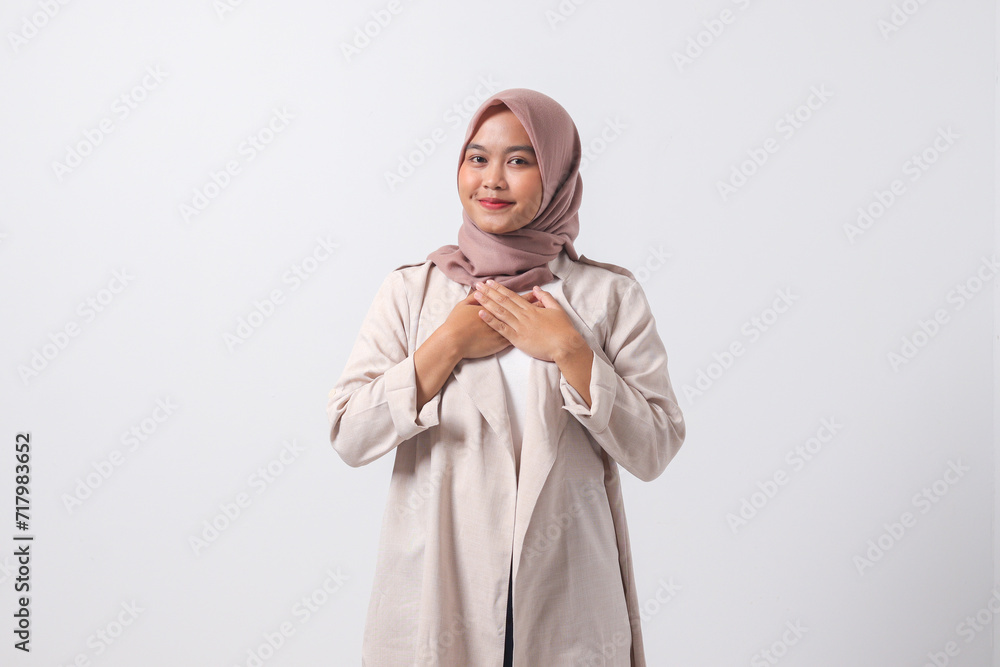 Portrait of excited Asian hijab woman in casual suit placing hand on chest and feeling peaceful. Mental health day concept, expresses sympathy and love, smiles positively. Isolated on white background