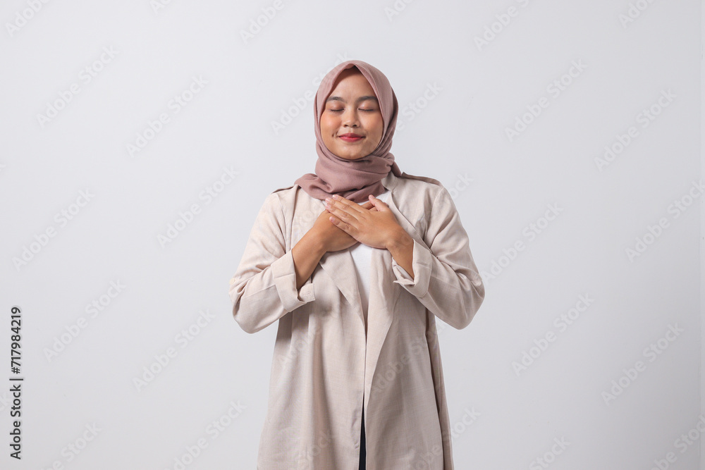 Portrait of excited Asian hijab woman in casual suit placing hand on chest and feeling peaceful. Mental health day concept, expresses sympathy and love, smiles positively. Isolated on white background Portrait of excited Asian hijab woman in casual suit placing hand on chest and feeling peaceful. Mental health day concept, expresses sympathy and love, smiles positively. Isolated on white background