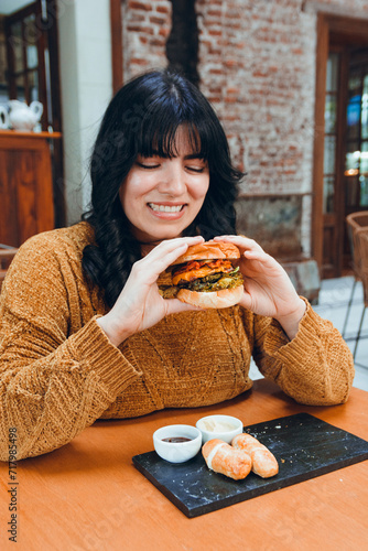 young woman excited eating big hamburger, vertical image for web and social networks of fast food