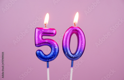 Pink and blue with white spots birthday candles burning on pink background. Number 50.	