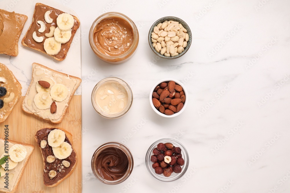 Toasts with different nut butters and products on white marble table, flat lay. Space for text Toasts with different nut butters and products on white marble table, flat lay. Space for text