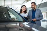 Couple at car dealership. Happy beautiful couple is choosing a new car at dealership. Happy young couple standing alongside their dream car and looking in