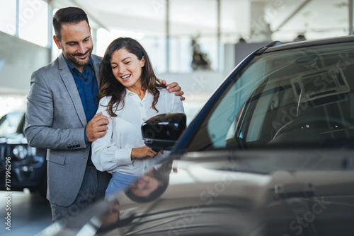 Portrait of a beautiful young couple choosing a new car at a car dealership. Buying a long-awaited car. Couple buying the car. Pair in a car salon. Husband with vife choose the automobile © Dragana Gordic