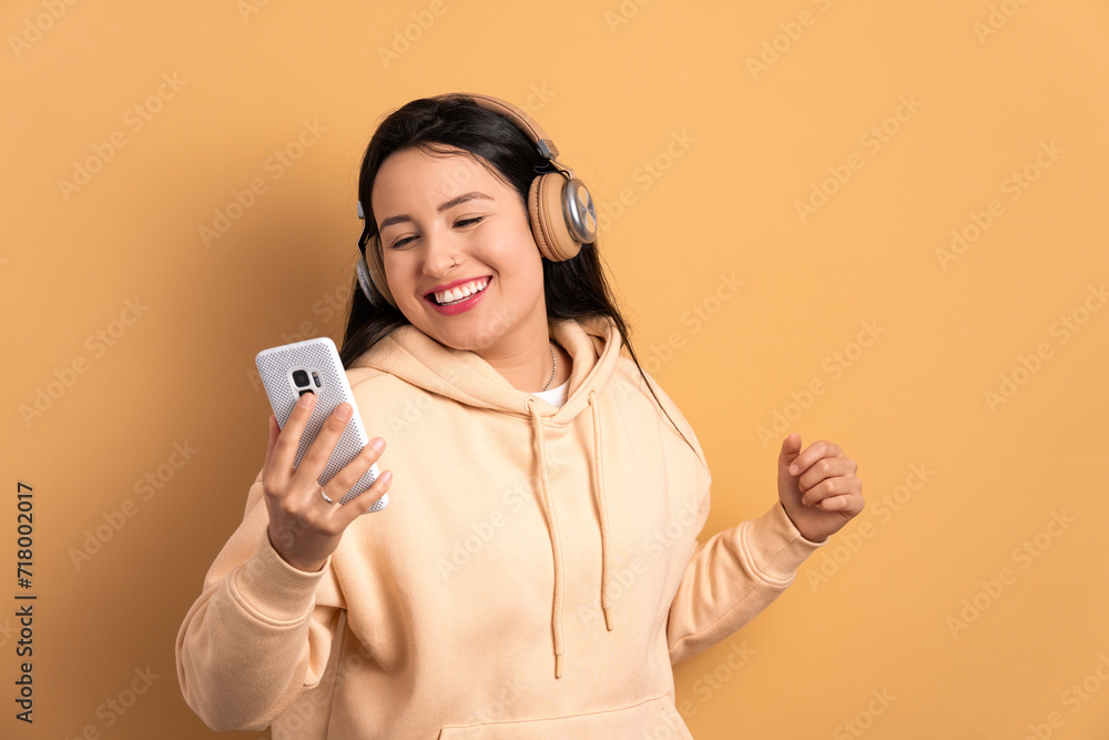 joyful young woman dancing with headphones in all beige colors. network, messaging, internet concept. joyful young woman dancing with headphones in all beige colors. network, messaging, internet concept.
