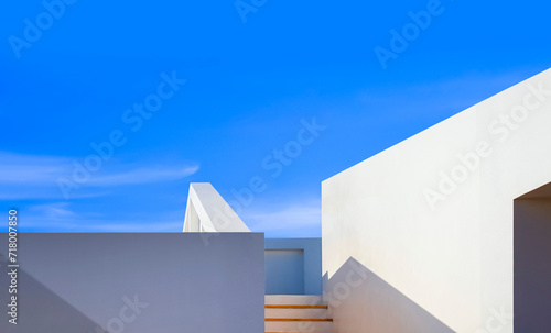 Minimal exterior geometric architecture background, rooftop and stairway of modern white building with sunlight and shadow on surface against blue sky