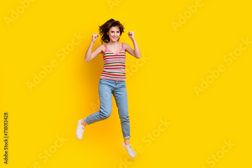 Full body photo of ecstatic satisfied girl wear striped tank fly clenching fists win lottery isolated on vibrant yellow color background