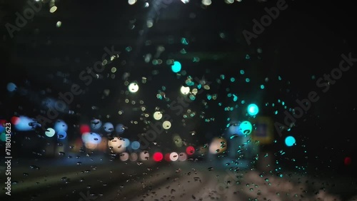 Winter night urban traffic scene as seen through the vehicle window covered with sleet drops. Melting snow water drips on the car windshield photo