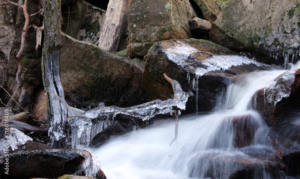 Fototapeta premium Dead branch covered in ice over a winter stream, Derbyshire England 