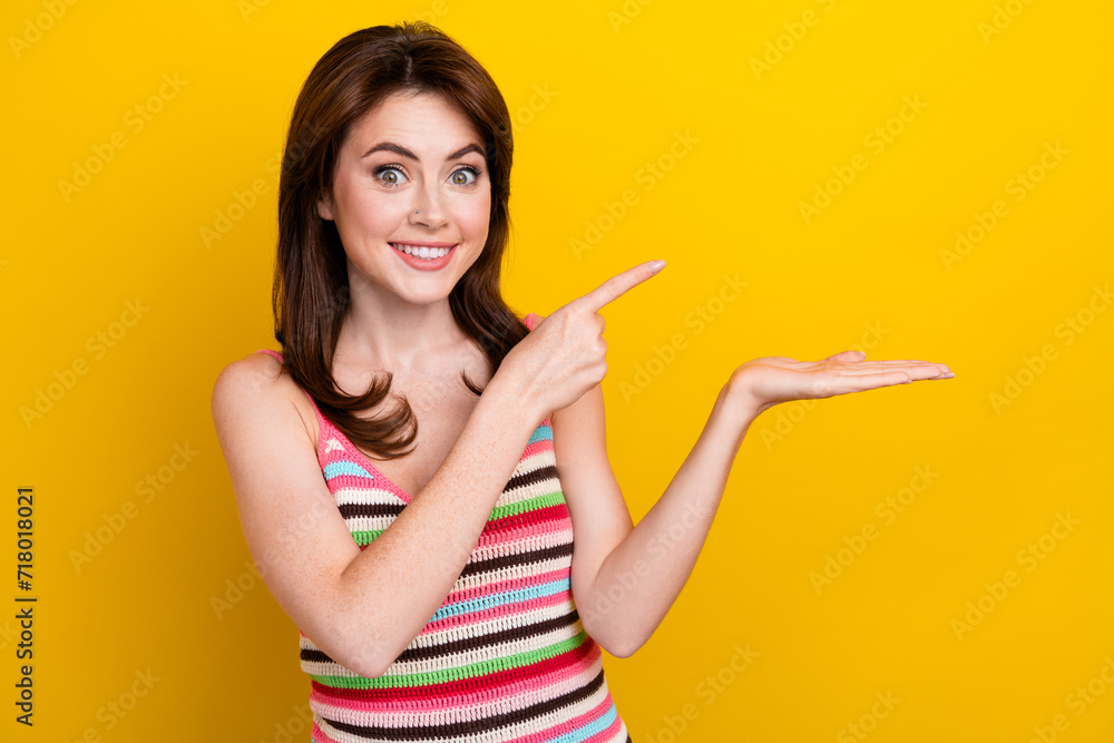 Photo of impressed lovely girl dressed striped top directing at promo empty space on hand isolated on vibrant yellow color background