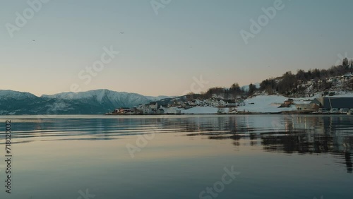 View of Ytre Samlafjorden in Norway, featuring clear waters, snowy mountains across the water, and homes nestled in the winter snow photo