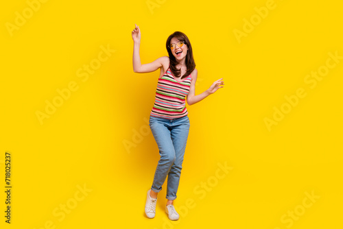 Full size photo of lovely woman dressed knitwear top jeans pants in sunglass dancing look empty space isolated on yellow color background