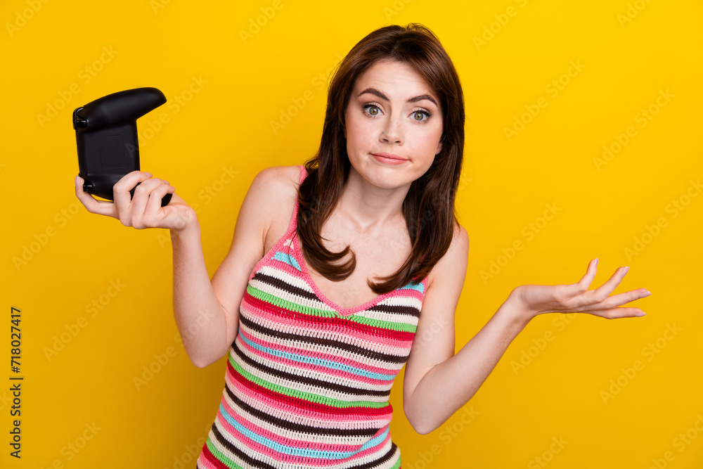Portrait of indifferent funny woman with long hair dressed knitwear top hold joystick shrug shoulders isolated on yellow color background Portrait of indifferent funny woman with long hair dressed knitwear top hold joystick shrug shoulders isolated on yellow color background