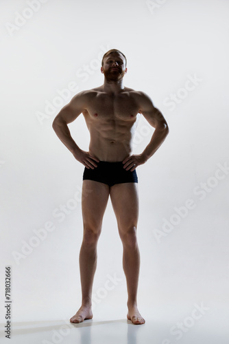 Full length portrait of young attractive man with perfect body curves posing in underwear against white background. Concept of natural beauty, aesthetic of body, male health, masculinity.