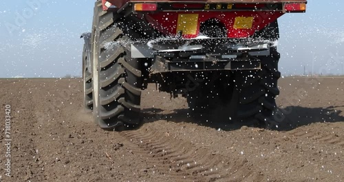 Farmer with agricultural machinery fertilizing agricultural field in spring time, slow motion. Spreading mineral fertilizer, cinematic low angle gimbal shot