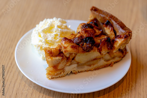 Selective focus of a piece of apple pie on white plate served with whipping cream on the side, Homemade apple pie on wooden table, Freshly baked.