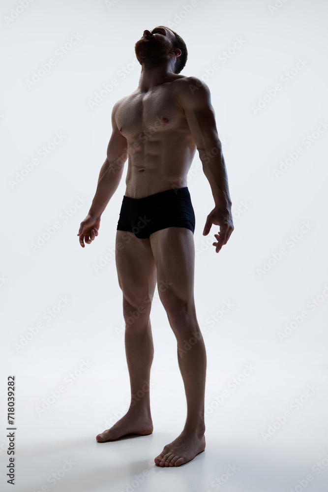 Young athlete man in underwear posing against white background. Male athlete model with naked torso and packs of abs. Concept of natural beauty, aesthetic of body, male health, masculinity.