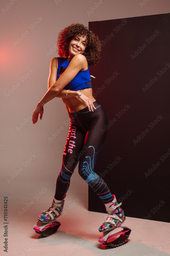 Sporty slim woman in leggings and top wearing kangoo jumper and posing in studio on background Sporty slim woman in leggings and top wearing kangoo jumper and posing in studio on background