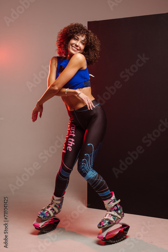 Sporty slim woman in leggings and top wearing kangoo jumper and posing in studio on background