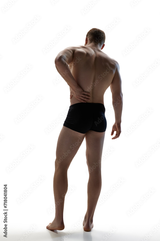 Scapula injury, loin inflammation, back pain. Muscular man put hand on hip against white studio background. Concept of natural beauty, aesthetic of body, male health, masculinity. Scapula injury, loin inflammation, back pain. Muscular man put hand on hip against white studio background. Concept of natural beauty, aesthetic of body, male health, masculinity.