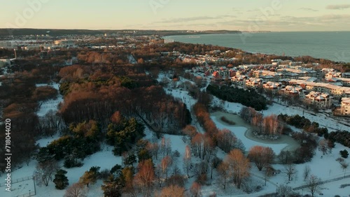 A view overlooking the forested areas of Przymorze shows the proximity to the coastline, with the Baltic Sea in the distance. The low angle of the sunlight bathes the scene in a warm, golden hu photo