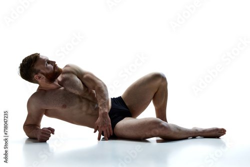 Full length portrait of young naked athlete man lying on floor against white background. Male model posing in underwear in studio. Concept of beauty care, male health, masculinity. Ad photo