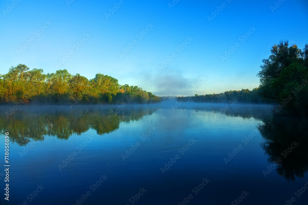 The Don River in the morning windless and foggy minutes. Sun is still behind floodplain forest, tops of trees are golden. The famous Russian novel by the writer Sholokhov is called the Quiet Don