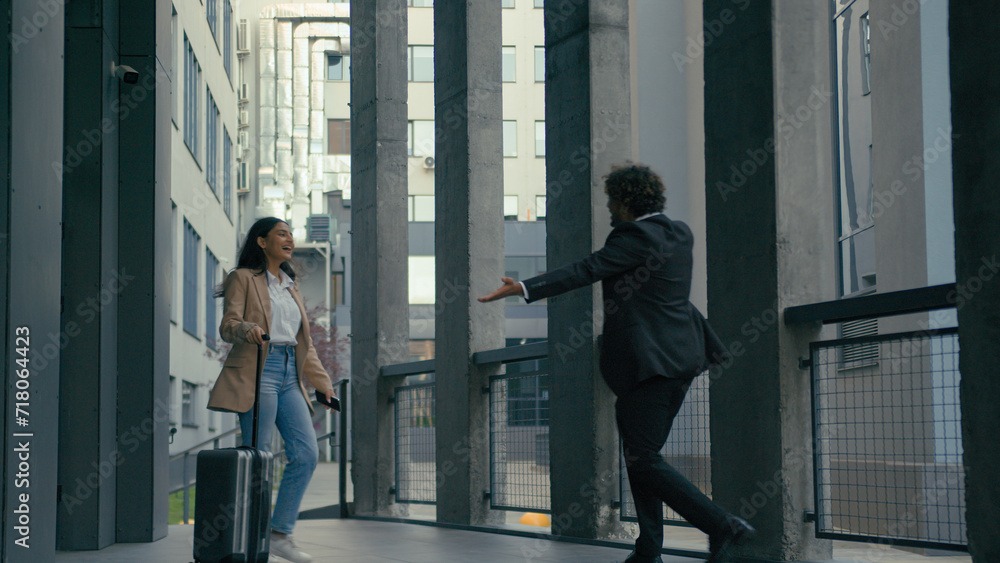 Fototapeta premium Indian businesswoman arrive in city with travel bag baggage luggage case Arabian businessman meet hug female partners business meeting in airport outdoors hugging colleagues coworkers friends greeting