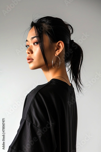 Beautiful Asian woman in a black T-shirt stands against a white wall, vertical photo