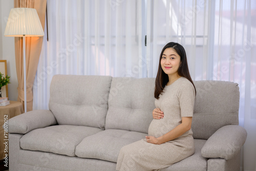 Asian pregnant woman sitting on sofa in living room at home Carrying a large belly She smiles looking at the camera and is happy at her home.