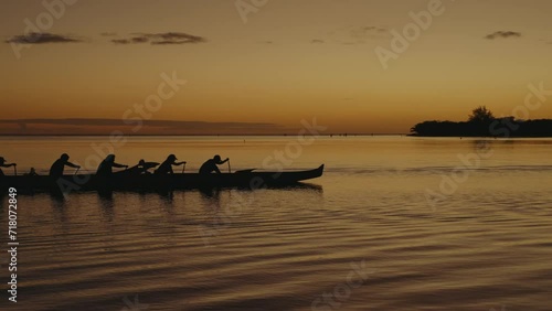 a  6 person  team paddles an outrigger canoe  or wa'a across a calm ocean in the Hawaiian islands at sunset as other boats follow behind silhouette photo