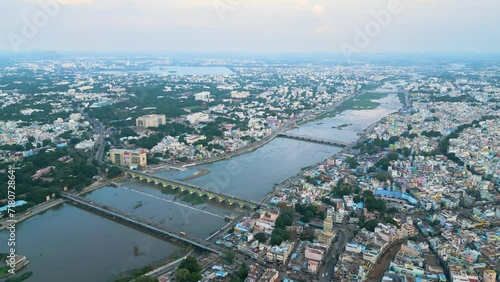 Ancient City of Madurai in Tamil Nadu, India. Dense, colorful Indian cityscape bisected by a river, bridge visible at dusk, aerial view.