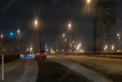 Cars is driving down a snowy street at night.