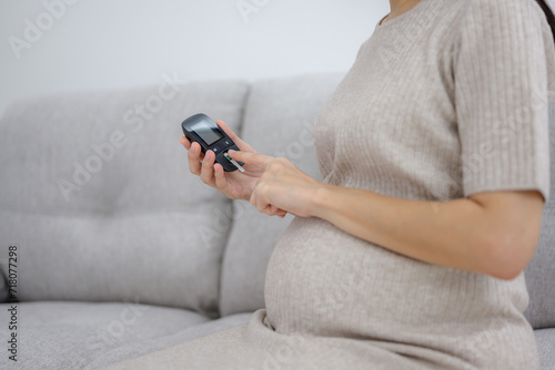 Pregnant women check their blood sugar levels before giving birth to check for diabetes before giving birth. Close-up shot of pregnant woman with diabetes sitting on sofa in living room. photo